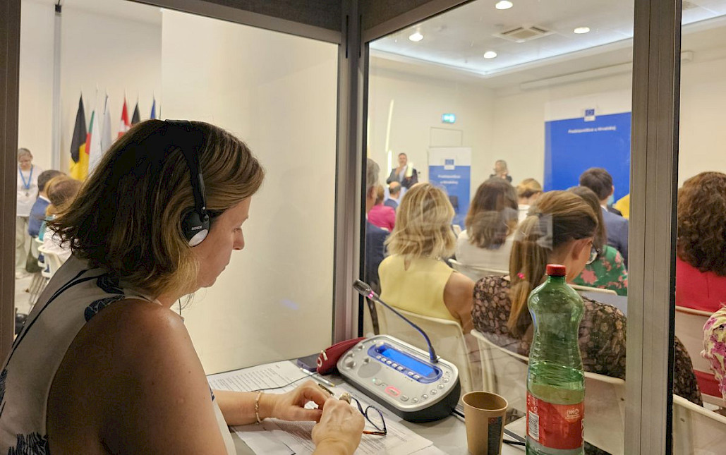 Konferencijski prevoditelj radi u kabini a u pozadini se vidi publika na konferenciji