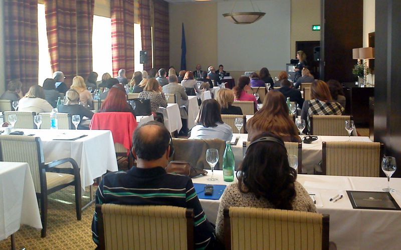 Smaller conference hall in school setup with participants at tables and speaker presenting at the front of the room