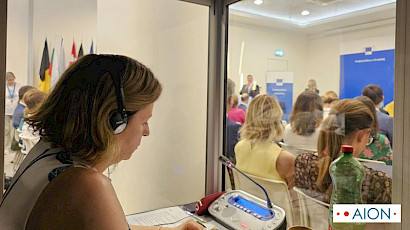 simultaneous interpreting inside an interpreting booth at a conference with audience in the background