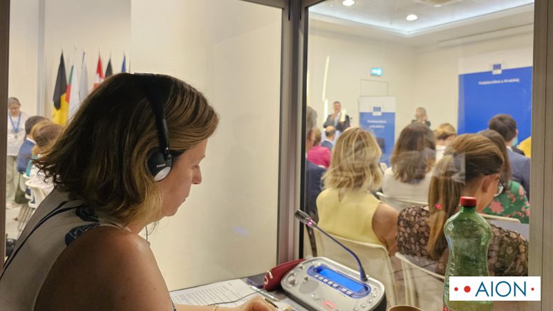 simultaneous interpreting inside an interpreting booth at a conference with audience in the background